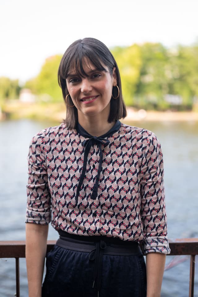 Tatjana Holter schaut lächelnd in die Kamera. Im Hintergrund sind ein Gewässer und Bäume erkennbar.