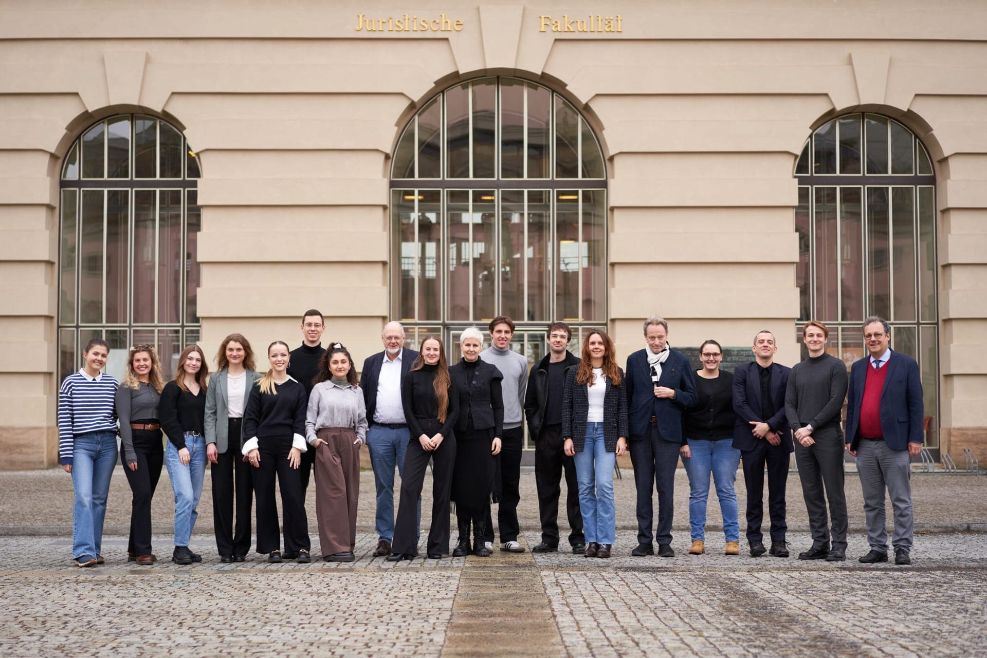 Vorstandsmitglieder, Betreuer:innen sowie Teilnehmer:innen der Law Clinics stehen vor einer sandfarbenen Gebäudefassade mit drei großen Fenstern.